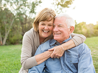 The image shows an elderly couple sharing a warm embrace outdoors during daylight hours.