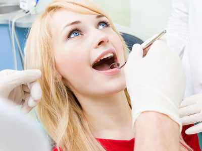 A woman with a surprised expression receiving dental care from a dentist.