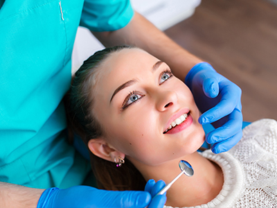 A smiling woman receiving dental care with a dentist using a mirror to examine her teeth.
